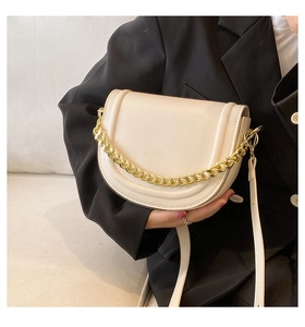 Detail of cream saddle bag with chunky gold chain and slim leather strap on model