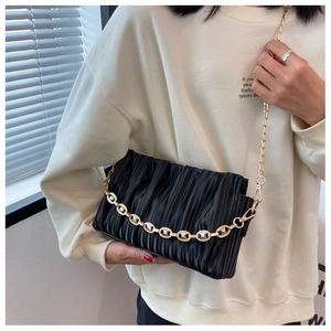 Detail of ruched black cloud bag with bold gold chain strap worn as a shoulder bag