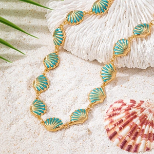 Golden seashell necklace with sky blue enamel on white sand and coral background