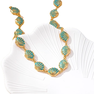 Golden sea shell necklace with teal enamel details displayed in a white seashell prop