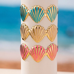 Dreiteiliges Muschel-Armreif-Set mit farbigem Emaille-Finish vor einem Strandhintergrund
