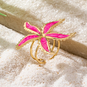 Macro shot of 3-layer gold ring with pink starfish enamel design on sand