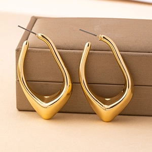 Macro shot of gold geometric earrings with irregular teardrop shape on brown leather box