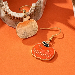 Cute Halloween pumpkin earrings with orange and black enamel face on festive orange backdrop