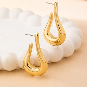 Boucles d'oreilles goutte d'or modernes aux lignes courbes sur un plateau en céramique