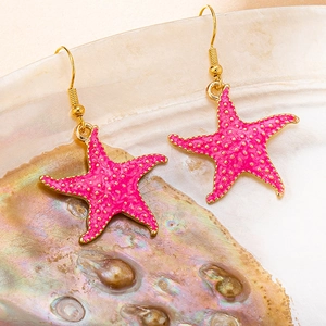 Detailed view of vibrant pink starfish earrings with gold trim resting on a seashell