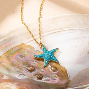 Colorful starfish pendant necklace in turquoise enamel with a gold chain in a shell