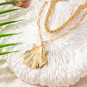 Double-layered golden necklace with beaded chain and rhinestone shell pendant on sand