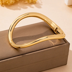 Macro shot of polished gold wave-shaped bangle with hinge on textured jewelry box