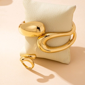 Polished gold organic bangle and ring set displayed on a beige textured jewelry pillow