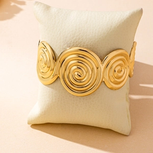 Polished gold wide spiral scroll cuff bracelet displayed on a premium cream jewelry pillow