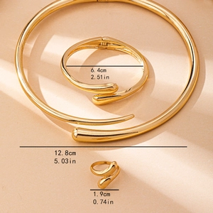 Parure de bijoux 3 pièces dorée avec collier ouvert, bracelet et bague sur fond de sable fin