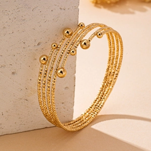 Macro detail of multi-layered gold bracelet with diamond-cut texture and polished beads