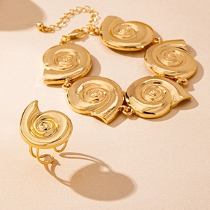 Detailed macro shot of a golden spiral snail shell jewelry set on a sandy surface