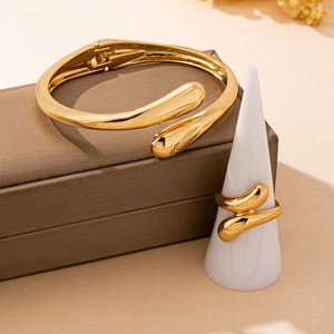 Polished gold cuff bracelet and matching ring set displayed on elegant jewelry stands