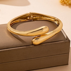 Makro-Detail des goldenen Tropfen-Armreifs mit poliertem Finish und Gelenk-Design