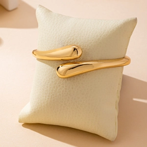 Schicker goldener offener Armreif mit Tropfenform und poliertem Finish auf Cremekissen