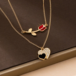 Détail de colliers dorés avec rose rouge et pendentif cœur pavé noir et blanc