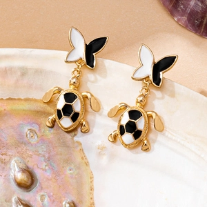 Detail of gold turtle earrings with black and white checkered enamel and butterfly studs