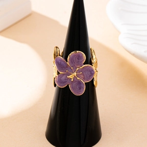 Bague dorée élégante avec fleur en émail violet sur un présentoir noir minimaliste