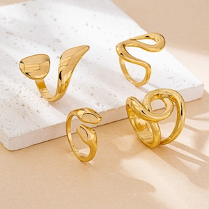 Close-up of four minimalist gold-plated rings with crossover designs on white marble