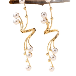 Elegant gold wavy tassel earrings with white pearls hanging on a wooden branch