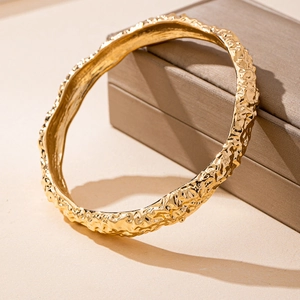Elegant gold metal bangle with irregular hammered texture on a brown jewelry box