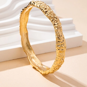 Close-up of golden irregular lava texture on an elegant geometric minimalist bangle