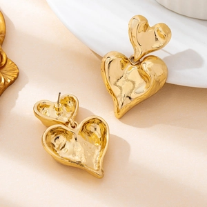 Golden double heart earrings with hammered texture finish on a minimalist beige background