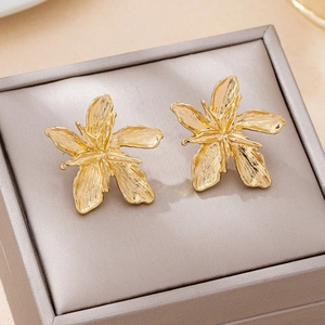 Macro detail of golden flower stud earrings with textured petals on gray velvet