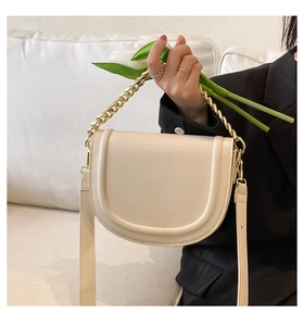 Close-up of beige saddle bag with gold chain handle and flowers in a soft lifestyle setting