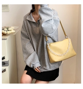 Close-up of light yellow leather bag with decorative chunky acrylic chain on grey hoodie