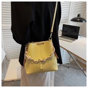 Close-up of yellow bucket bag with chain strap and decorative silk scarf accessory