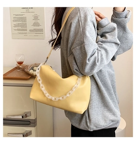 Detail of yellow underarm bag with thick white acrylic chain and zip closure on grey sweater