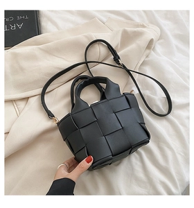 Macro shot of black woven leather handbag showing wide strap texture and minimalist handle