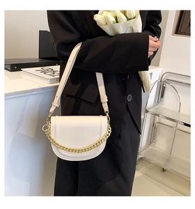 Detail of a chic cream saddle bag with chunky gold chain and slim leather shoulder strap