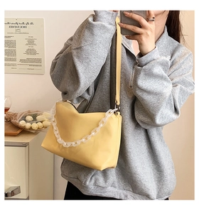 Detail of light yellow trapezoid shoulder bag with white acrylic chain and zip closure