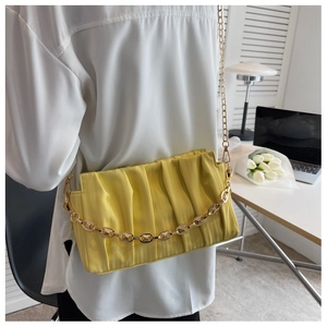 Detail of yellow pleated shoulder bag featuring a gold chain strap worn by a model