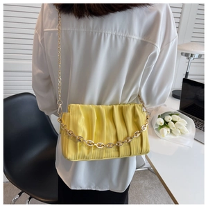 Detail of yellow pleated shoulder bag with gold chain strap shown in a modern interior