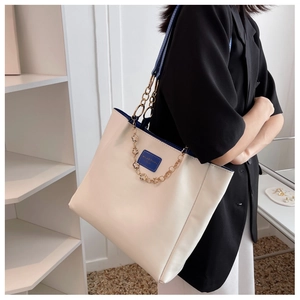 Detail view of cream tote bag featuring blue contrast piping and golden floral chain handle