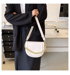 Close-up of beige saddle bag with gold chain decoration and adjustable wide strap
