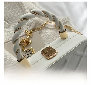 Close-up of white quilted leather bag featuring a gold turn-lock and woven chain strap
