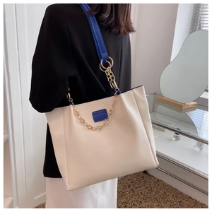 Detailed shot of beige leather tote bag with blue strap and gold chain detail on model