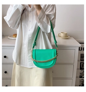 Detail of green leather saddle bag with chunky gold chain strap and adjustable belt