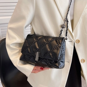 Chic black quilted shoulder bag with silver chain and metal ball detail on white suit