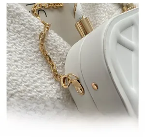 Macro shot of polished gold metal hook and quilted white leather on the chain handbag