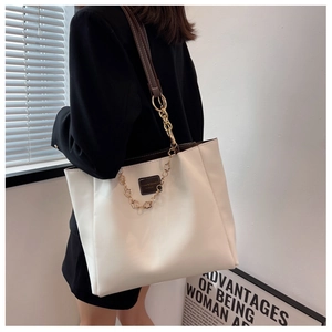 Detailed view of white minimalist tote bag with gold chain and dark leather strap on shoulder