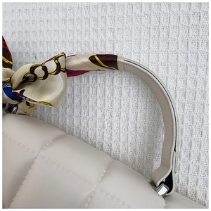 Close-up of white quilted handbag featuring a decorative silk scarf wrapped around the handle