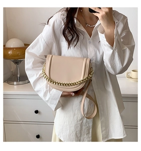 Detail of a beige saddle bag with a chunky gold chain and adjustable leather strap