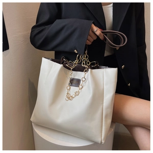 Detail of a large tote bag with contrast stitching and floral metal chain ornament